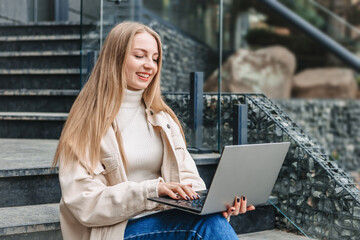 Happy student girl sitting on stairs near office center with laptop smiling and studying. online education