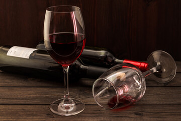 Two bottles of red wine with two glasses on an old wooden table. Focus on an overturned glass of wine