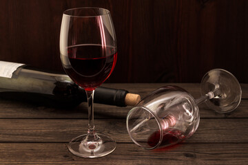 Bottle of red wine with two glasses on an old wooden table. Focus on an overturned glass of wine
