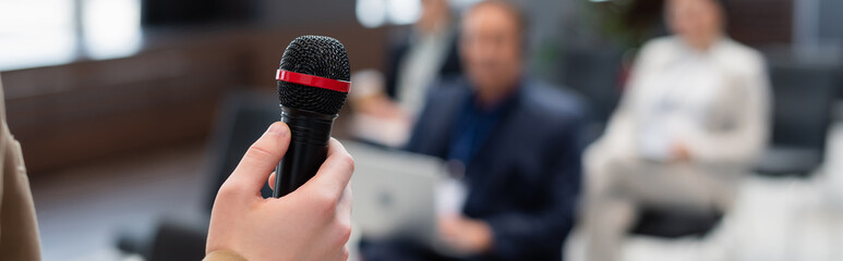 lecturer holding microphone near blurred audience during seminar, banner