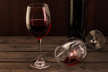 Bottle of red wine with two glasses on an old wooden table. Focus on an overturned glass of wine