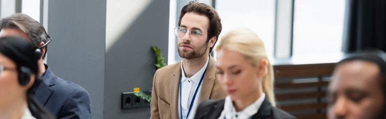 Businessman looking away near multiethnic colleagues in headsets during conference, banner