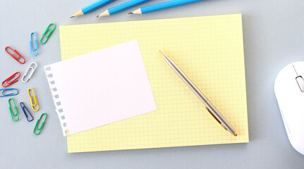 Notepad with blank space for text on a gray background next to pencils and paper clips.