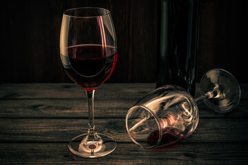 Bottle of red wine with two glasses on an old wooden table. Focus on an overturned glass of wine