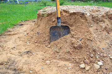 Shovel in a pile of construction gravel on a garden plot, side view, close-up