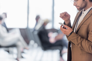 Cropped view of businessman using smartphone near blurred conference room