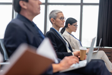Asian businesswoman using laptop near blurred colleagues in conference room