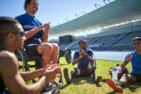 Paraplegic and amputee male athletes clapping on sunny stadium grass 