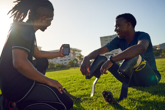 Coach with smart phone talking to amputee athlete in sunny grass
