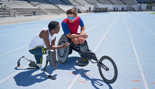 Male amputee and wheelchair athletes talking on sunny blue track