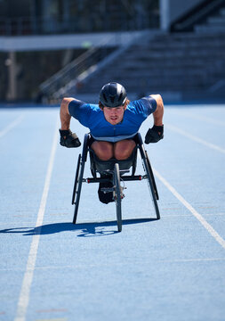 Focused male wheelchair athlete training on sunny blue sports track