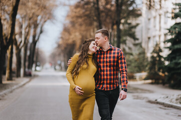 A smiling man in a red plaid shirt and a pregnant woman in a yellow dress are walking along the...