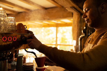 Male barista preparing cappuccino at espresso machine in cafe