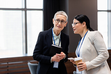 Multiethnic businesswomen with notebook and smartphone talking in office