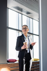 Mature businesswoman holding cellphone and coffee to go