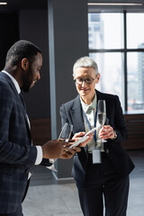 interracial business partners with champagne glasses and smartphones talking in office
