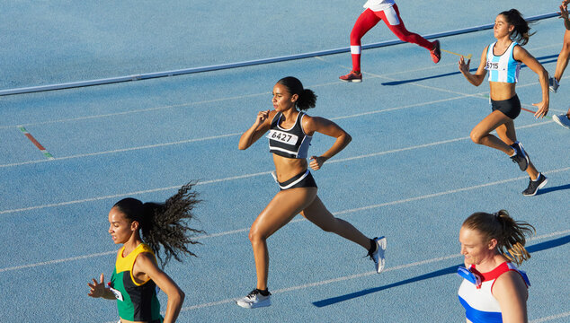Female track and field athletes running in competition on blue track