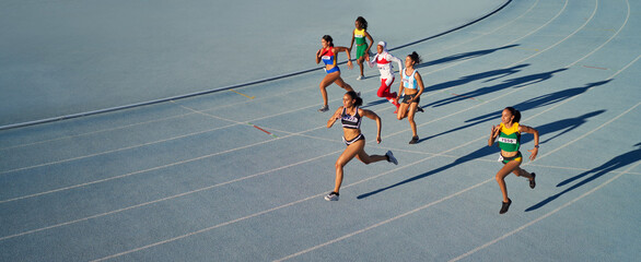 Female track and field athletes running in race on blue track