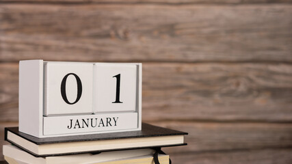 Cube wooden calendar on a pile of books, on first day of January with wooden background.