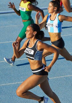 Female track and field athletes running on sunny track