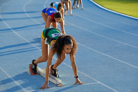 Female track and field athletes ready at starting blocks on blue track - Powered by Adobe