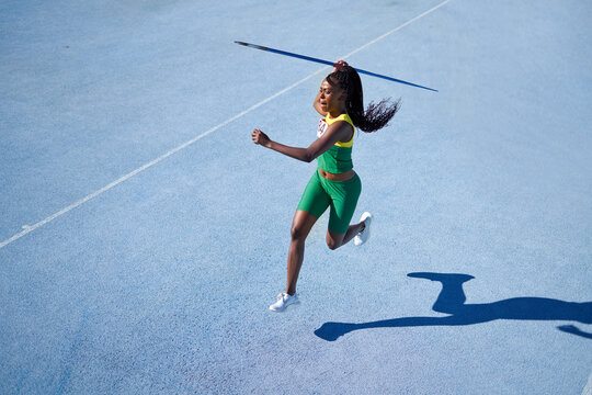 Female track and field athlete throwing javelin on sunny blue track