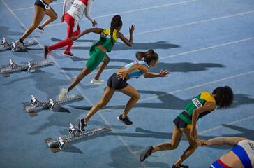 Female track and field athletes taking off from starting blocks