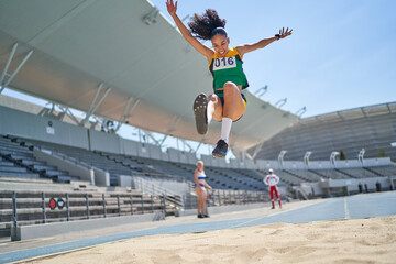 Female track and field athlete long jumping over sand