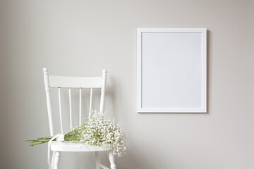 16x20 thin white vertical frame mockup template, hanging on a neutral coloured wall. Fresh bunch of flowers flowers sitting on an old, white, rustic chair.