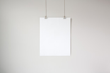 Vertical hanging poster mockup on a neutral coloured wall. Hanging by clips and string. 4:5 aspect ratio poster.