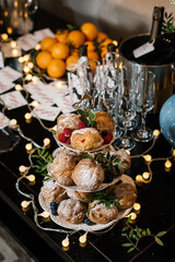 Fototapeta na wymiar buffet table with glasses prepared for champagne and a slide with profiteroles, decorated with blueberries, raspberries and green leaves. small bulbs lie on the table