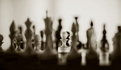White pawn and silhouettes of chess pieces. Wooden chess pieces on the chessboard.