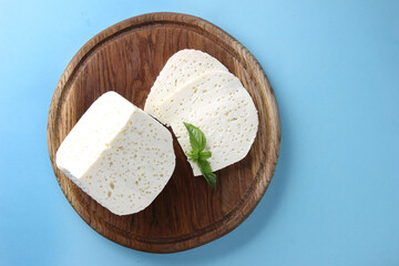 Homemade cheese with basil on a wooden board on a bright blue background. Flatlay, top view. Background image, copy space