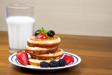breakfast table with honey pancakes, strawberries and blackberries in the background a glass of milk