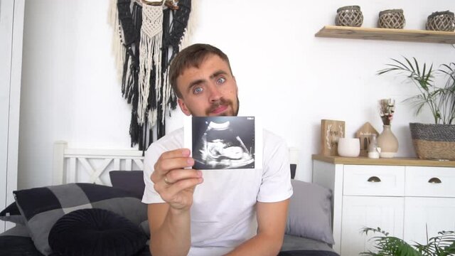 Slow Motion Young father holding ultrasound photo of newborn baby, maternity and family concept