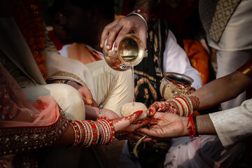 A scene from Indian hindu wedding where water is being poured out on hands from a vessel.
