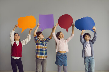 Naklejka premium Children of new generation express opinions. Group of cute junior kids holding up multicolored clean paper bubbles. Happy smiling elementary school boys and girls with text bubbles standing in studio