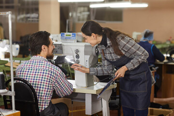 Two factory workers talking at table with industrial shoe sewing machine. Workshop manager...