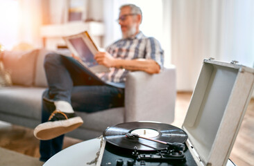 A mature man sits on the couch at home, relaxes, enjoys life and listens to vinyl records on a...