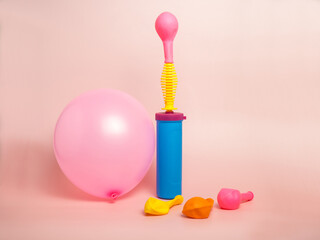 Plastic hand pump next to the pink balloon with . Preparing for the holiday. Organization of the birthday party. Decorator tool on a pink background