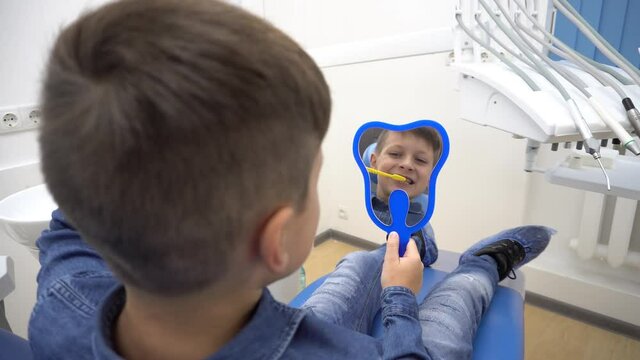 4K Little boy sitting in dantist chair with mirror. Male patient look at his tee