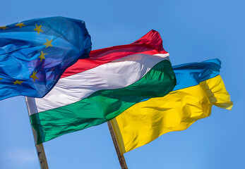 Flags of Hungary Ukraine and European Union waving on pole against blue sky