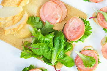 Cream cheese sandwiches with red fish, baguette, iceberg lettuce leaves, swiss chard on wooden board, top view