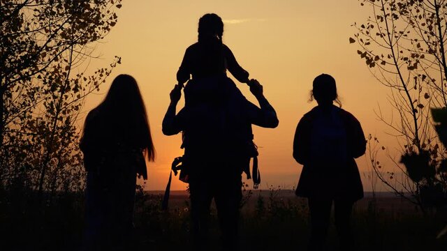 Family sunset black silhouette. Silhouette of running family. People are walking together holding hands across field. Parents with children hold hands together. Black silhouette of people in field.