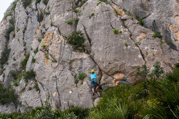 Climber equipped with helmet and ropes, ascending the rocky wall of a mountain. 