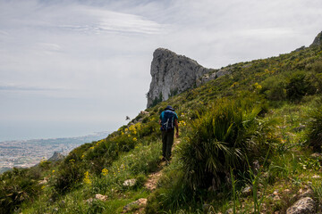 Hiker equipped with a backpack, walking through a rugged and stony mountain, on a morning with cloudy skies, in Sierra de Segaria, Alicante (Spain).