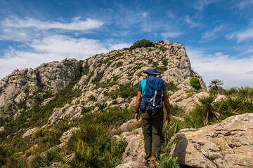 Fototapeta premium Hiker equipped with a backpack, walking through a rugged and stony mountain, on a morning with cloudy skies, in Sierra de Segaria, Alicante (Spain).