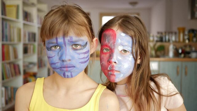 Two children kids girls at home posing with painted faces body art having fun together