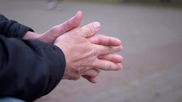 Seated Male Rubs Warm Hands Outdoors in the Park. Moment of expectation, excitement, anxiety. Strong, working man hands. Close up. Slow-motion. Slow motion. 180 fps.