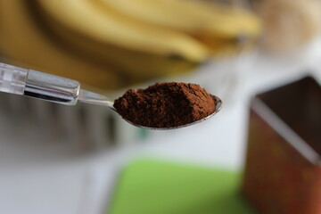 Ground coffee in a spoon. Bananas in the background. Blurred background